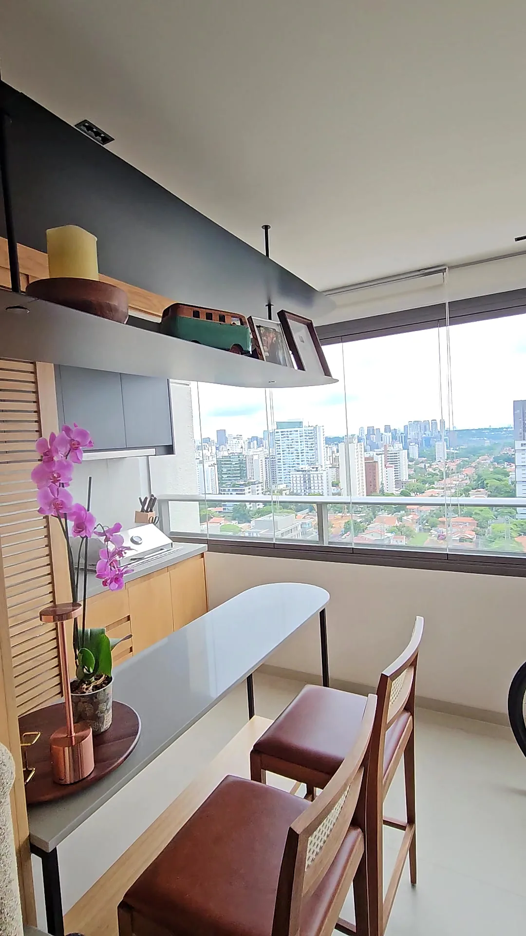 Varanda gourmet com banquetas de couro, orquídea e vista da cidade