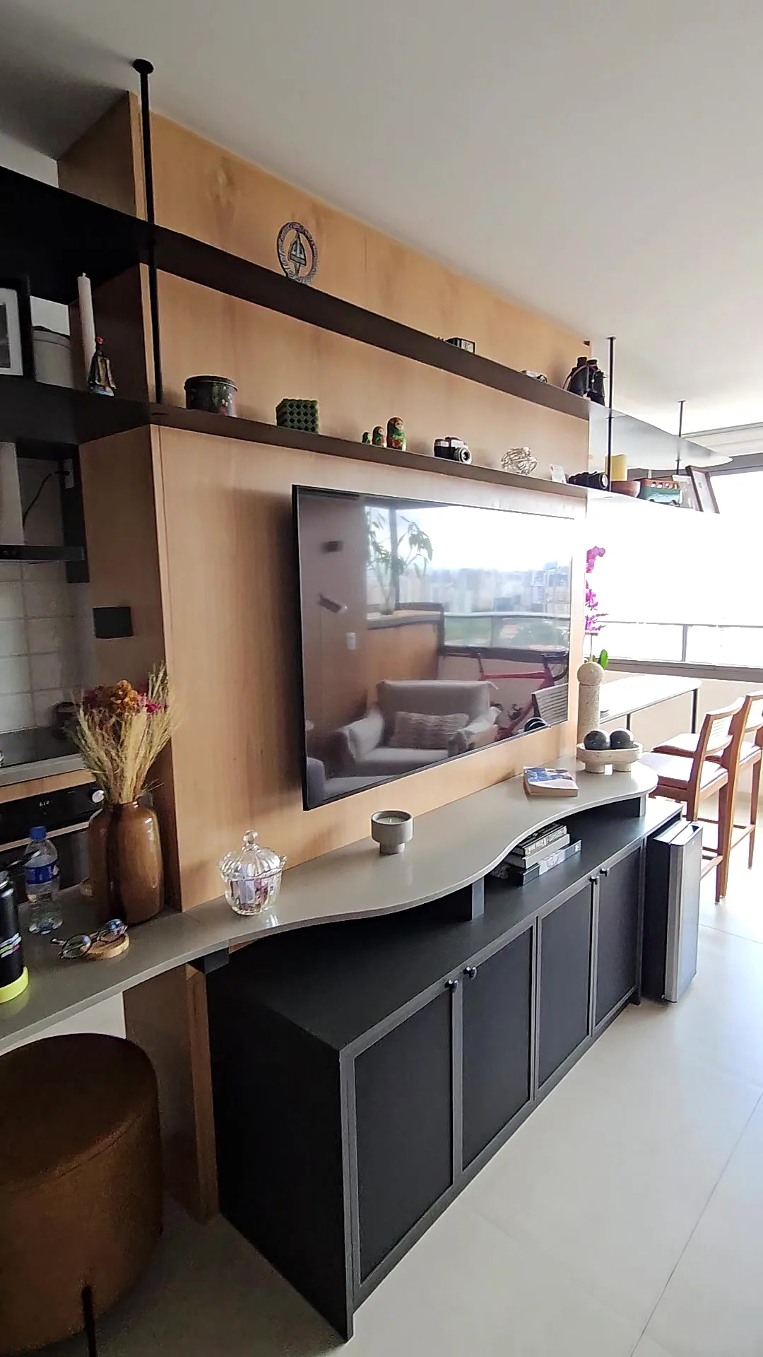 Sala com painel de madeira para TV, prateleiras e cozinha integrada