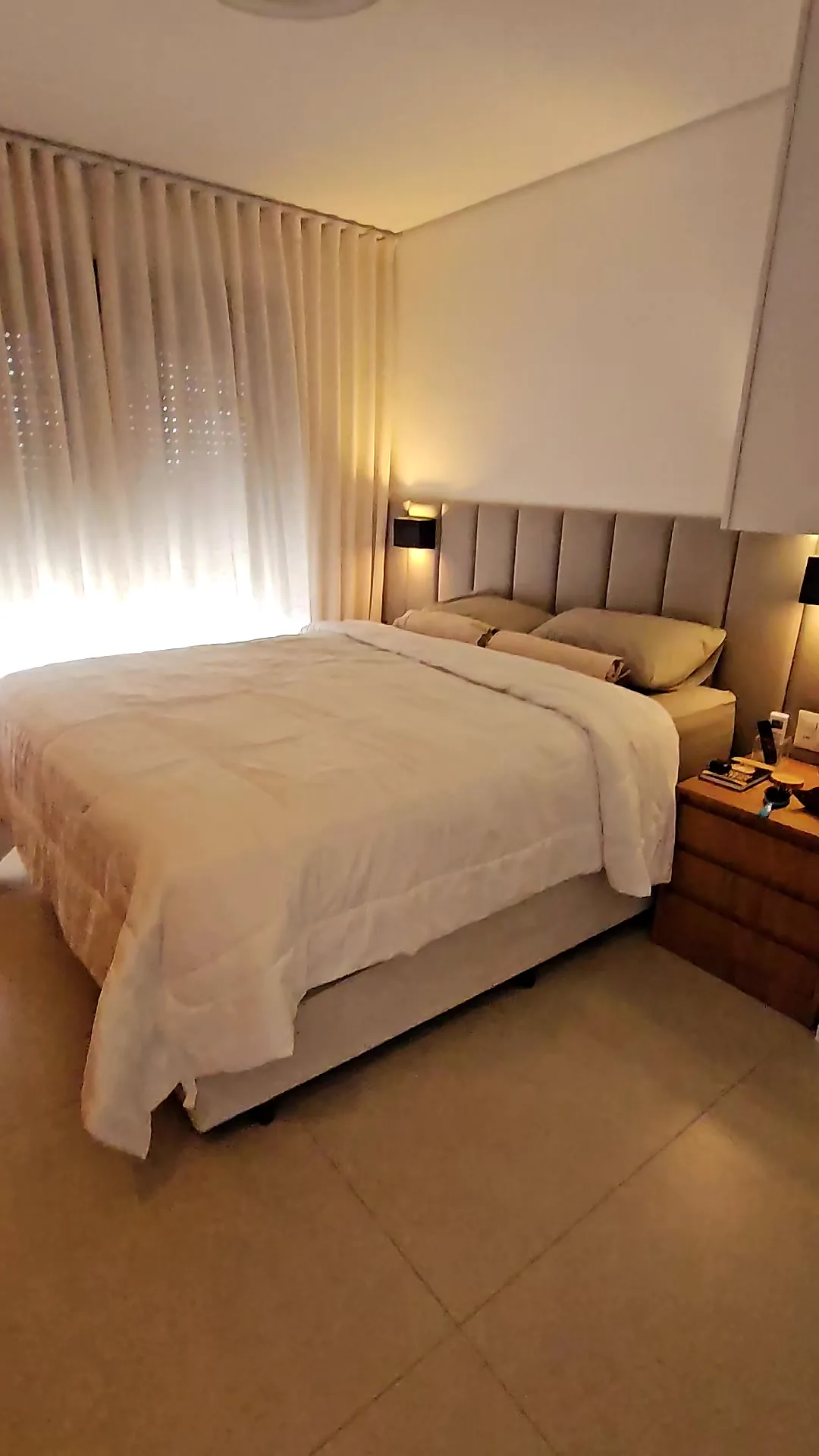 Quarto com cabeceira estofada, luminárias de parede e cortina clara